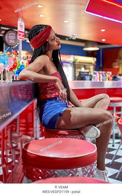 Young woman with braided hairstyle sitting on a bar on red stool