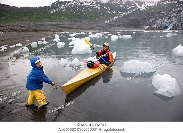 Young child helps pull in kayak as father finishes kaying in Shoup Bay State Marine Park, Prince William Sound, Southcentral Alaska