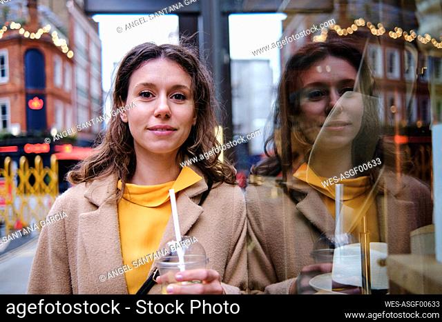 Woman with juice glass leaning on window of store