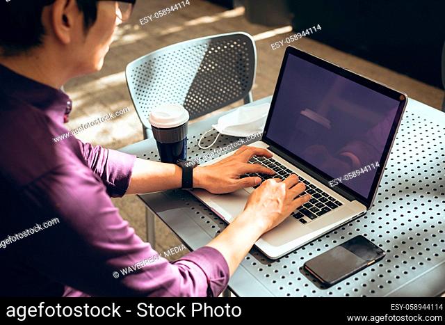 Asian businessman using laptop with blank screen sitting at table in cafe
