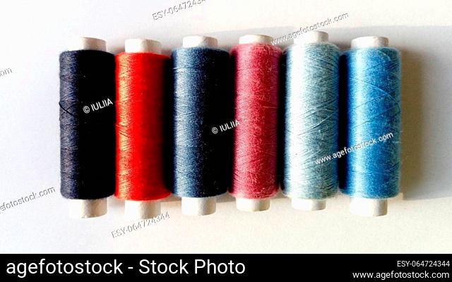 Baboons and spools of thread in different colors. Close-up. Natural light on one side. White background. Blue, red, pink, gray, black
