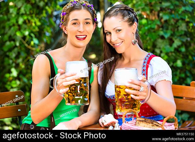 In Beer garden ??female friends in Tracht, Dirndl and Lederhosen drinking a fresh beer in Bavaria, Germany