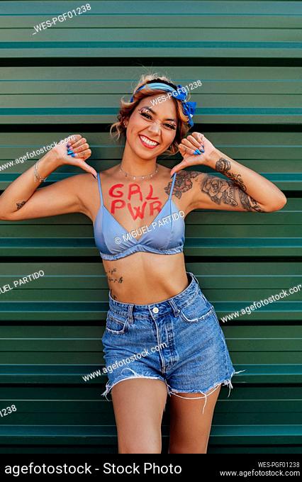 Smiling woman with girl power text on chest in front of wall