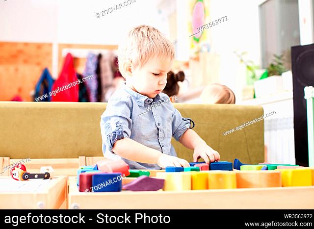 Cute blond boy playing with colorful wooden cubes