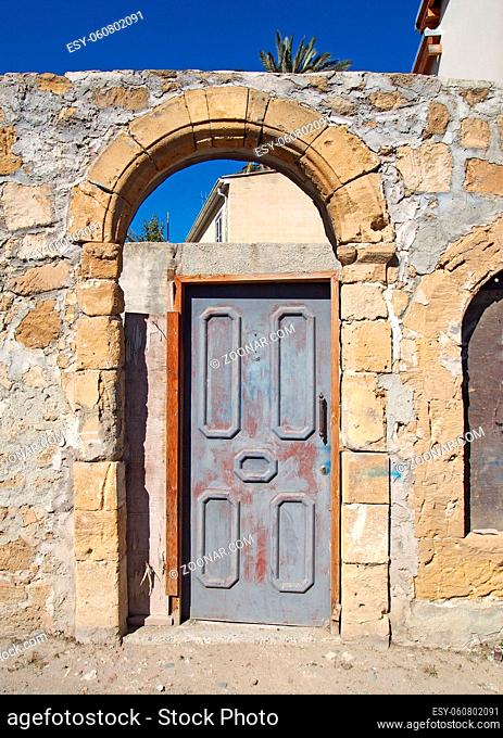 an old wooden door in an arched frame in an ancient stone wall on a sunlit street in nicosia cyprus