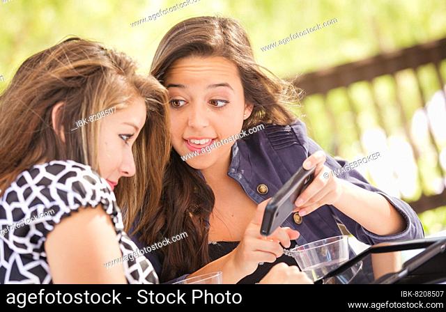Expressive young adult girlfriends using their computer electronics outdoors