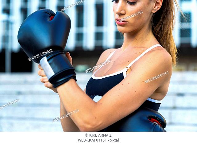 Sportive young woman putting on boxing gloves in the city