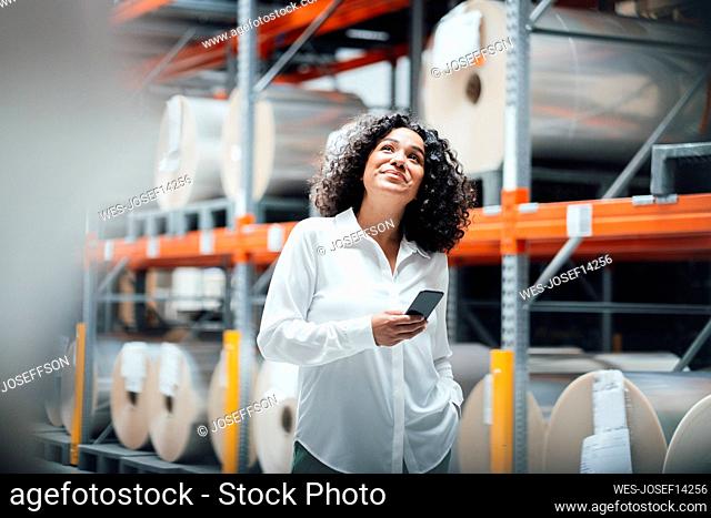 Smiling businesswoman with smart phone standing in front of rack