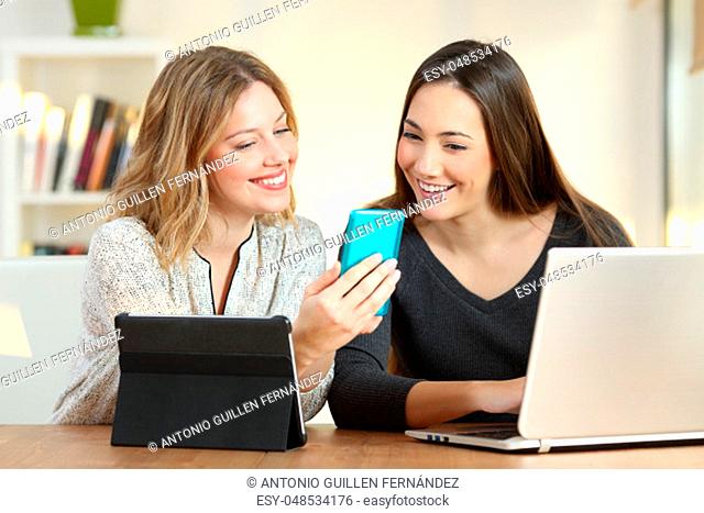 Two happy girls checking information in multiple devices at home