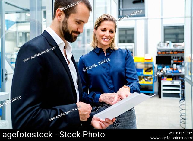 Smiling businesswoman discussing with businessman holding document at factory