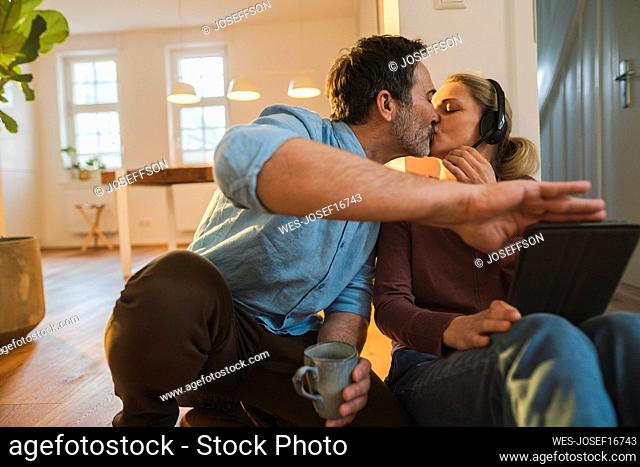 Affectionate husband kissing wife wearing headset at home office