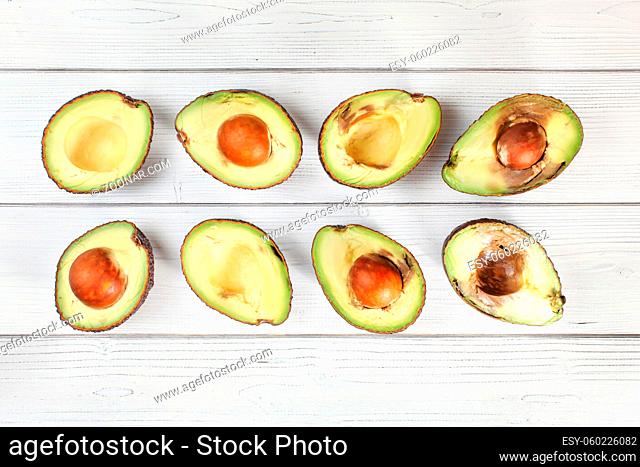 Avocado halves on white boards desk, view from above. Fruits arranged from unripe to overripe