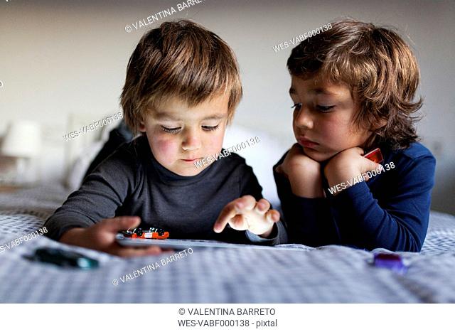 Two little boys lying on bed playing with digital tablet