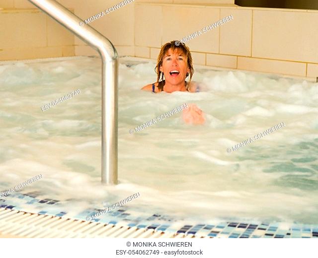 A woman in a Jacuzzi. She looks out of the water laughing with her head, in the foreground the toes look out of the water