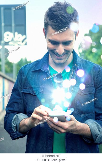 Young man texting on smartphone with glowing lights coming out of it