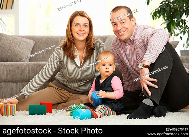 Happy family sitting on floor smiling at camera with baby girl