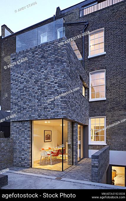 Overall dusk view of double-height rear extension with corner window on ground level. Queens House, London, United Kingdom