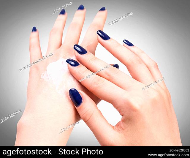 Beautiful female hands with cream over gray background