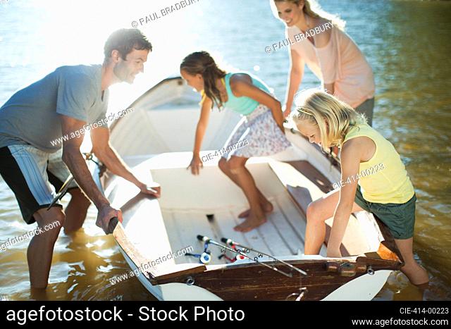 Family getting into rowboat with fishing rods on lake