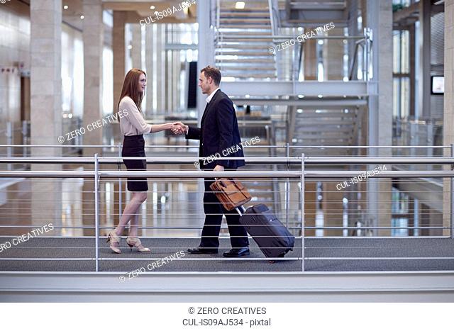 Mid adult businesswoman greeting businessman on conference centre walkway