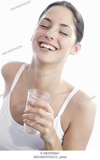 Young woman holding glass of water, eyes closed, smiling, close-up