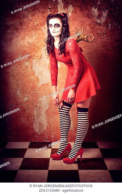 Grunge photograph of a drained weak and powerless human wind-up doll wearing sugar skull make up with retro red dress and metal turn dial key on back