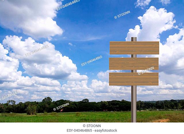 Blank wooden sign in green grass field over blue sky background
