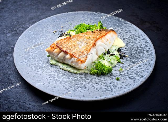 Modern style traditional fried skrei cod fish filet with mashed potatoes and baby broccoli served as close-up on ceramic design plate with copy space