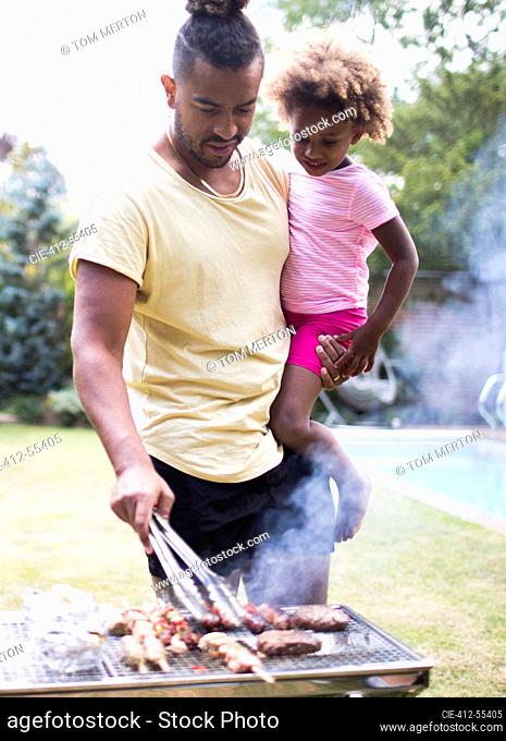 Father holding daughter at barbecue grill in summer backyard