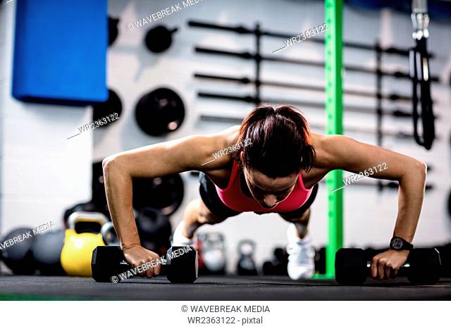 Determined woman doing push ups with dumbbell