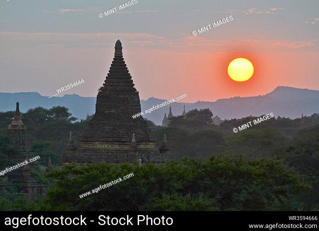 Sunset over distant mountains with stupa of temple in the foreground, Bagan, Myanmar