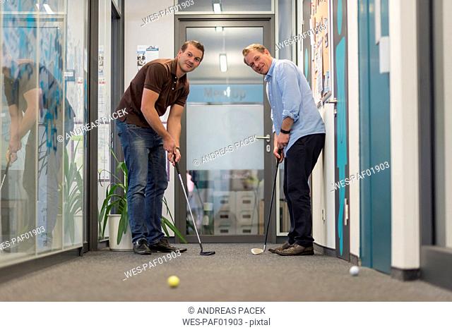 Two businessmen playing golf in office