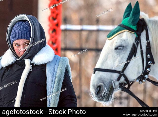 RUSSIA, VLADIMIR REGION - DECEMBER 8, 2023: A woman is seen by a horse-drawn carriage in the town of Suzdal on a frosty winter day