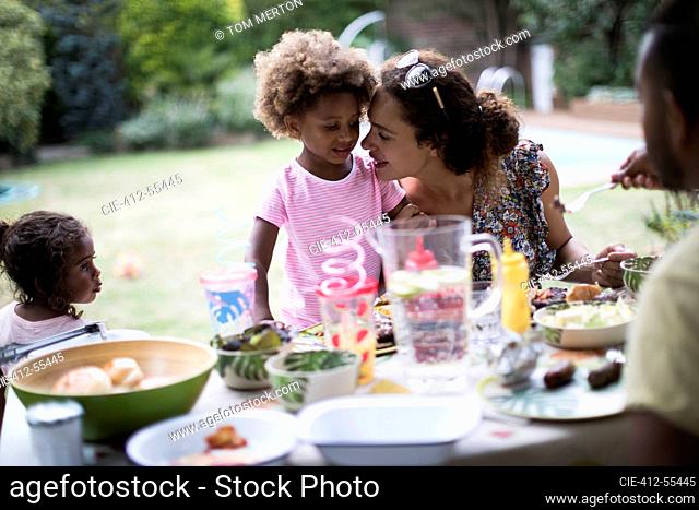Mother and daughter enjoying backyard barbecue at patio table