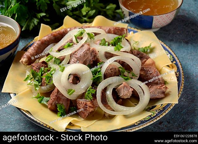 Beshbarmak - National Kazakh dish, prepared with meat and pasta. Beshbarmak dish close-up on a plate on the table. Large pieces of stewed meat and onion