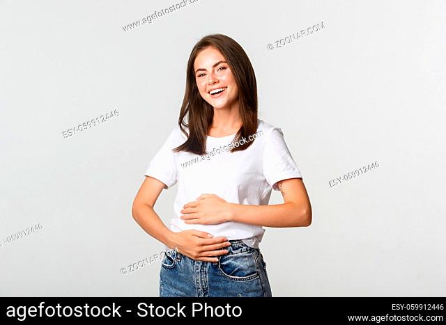 Satisfied smiling brunette girl rubbing belly after eating delicious food
