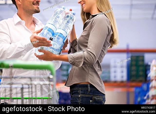 Happy young couple shopping for pure packed bottles at supermarket