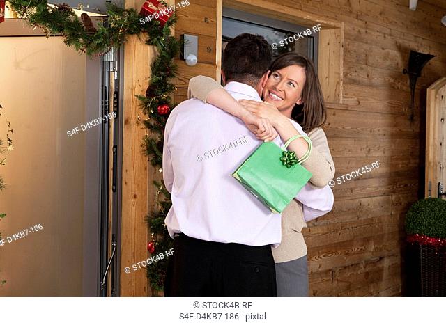 Couple with Christmas present embracing at wooden house