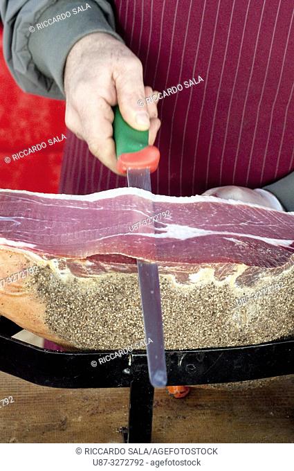 Italy, Umbria, Norcia, Stall Market, Market Stall Trader Carving a Ham. . .
