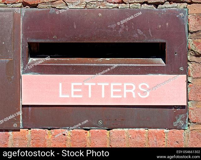 an old british postal mail box in a brick wall with rusted metal surround and the word letters on a faded red panel