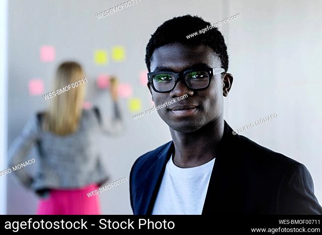 Young businessman smiling with female colleague in background at office