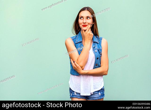 Happy cheerful teenage girl with freckles, casual style white t shirt and jeans jacket, looking up, thinking and touching her face and a