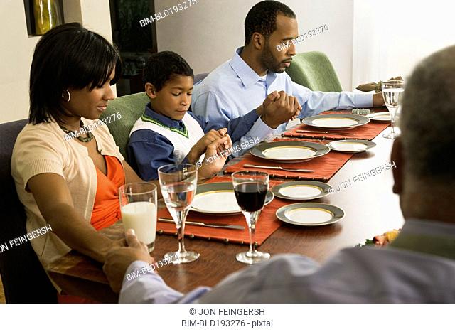 African American family saying grace at dining table