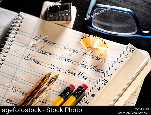 Black Lives Matter slogan written on a school calligraphy notebook, next to him rubber, pencil, pencil sharpener, pen and vision glasses