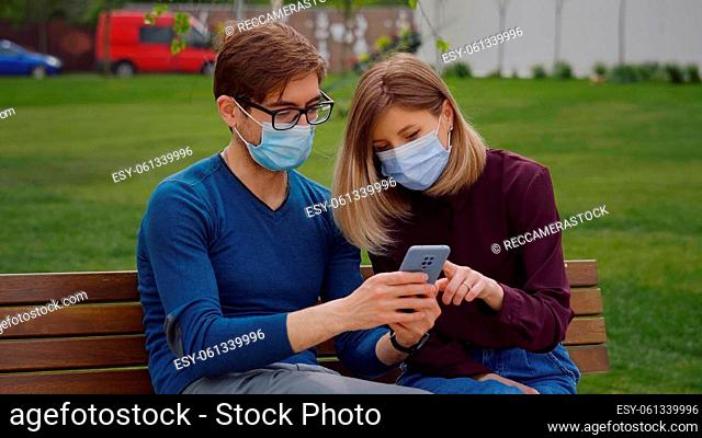 Two cute people look closely on phone and find out from news Couple sitting on bench, green background