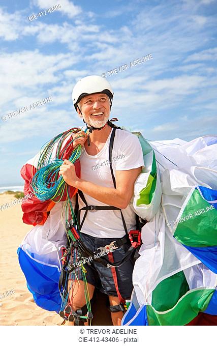 Smiling mature male paraglider carrying equipment and parachute
