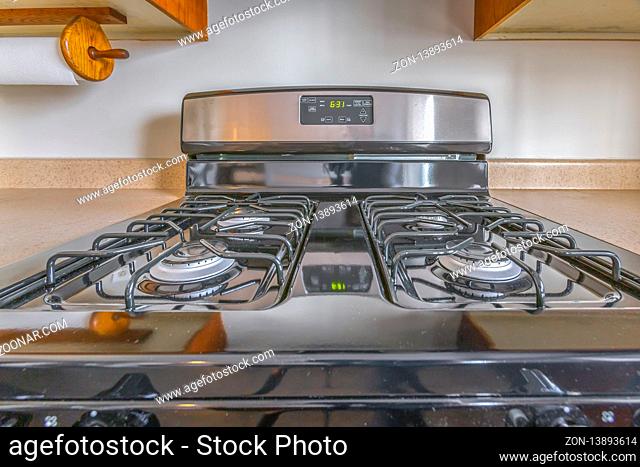 Close up of a gas stove with a shiny surface inside the kitchen of a house. Cabinets and tissue holder is mounted on the wall above the stove and countertop