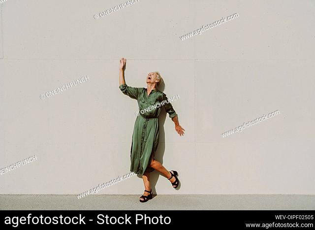 Mature woman laughing in front of white wall on sunny day