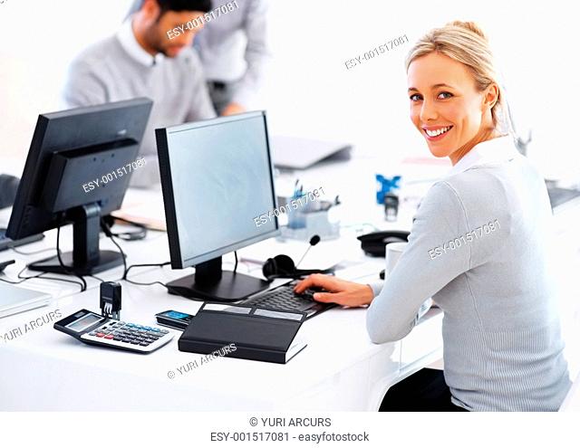 Portrait of smiling business woman at desk using computer with colleagues in background