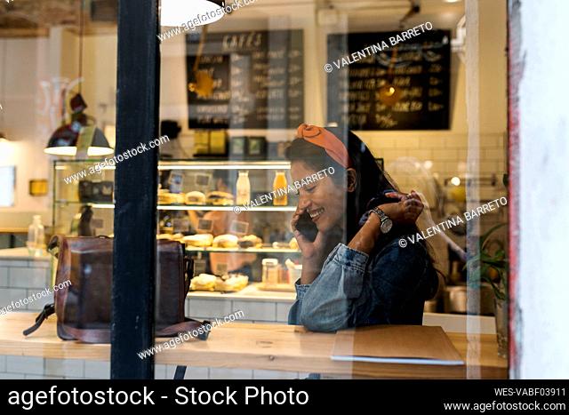 Smiling young woman talking on mobile phone while sitting at cafe